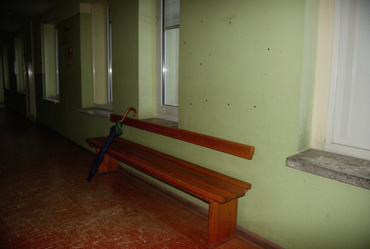 Pusty korytarz biurowca z drewnianą ławką i zielonymi ścianami jesienną porą